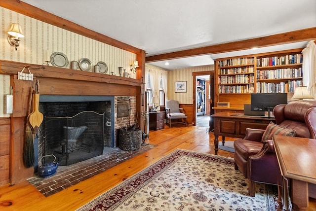 living room with hardwood / wood-style flooring, beamed ceiling, a brick fireplace, and wallpapered walls