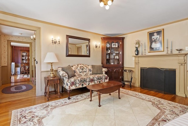 living area with light wood-type flooring, a fireplace, ornamental molding, and wainscoting