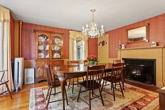 dining room with wallpapered walls, light wood-style floors, radiator, a chandelier, and a wainscoted wall