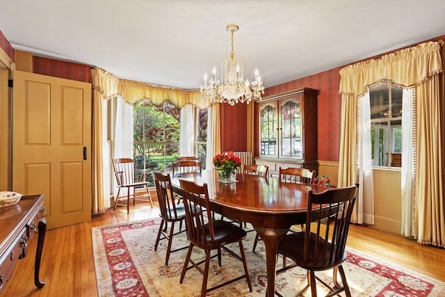 dining room with a chandelier, healthy amount of natural light, light wood-type flooring, and a wainscoted wall