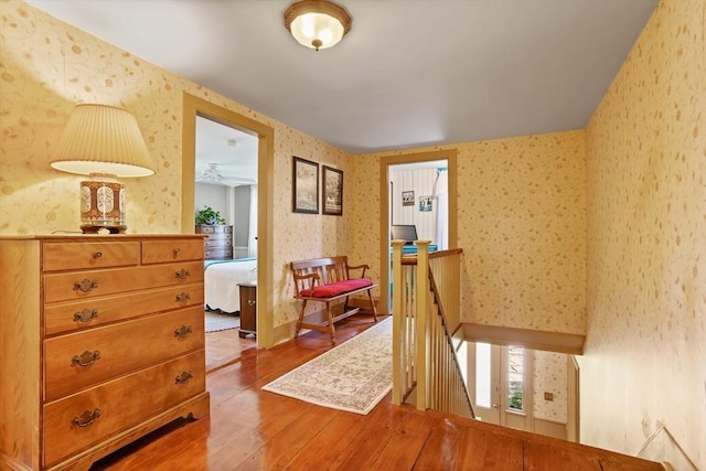 corridor with wallpapered walls, an upstairs landing, and hardwood / wood-style flooring