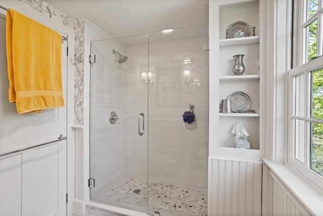 full bathroom with a stall shower, built in shelves, and healthy amount of natural light