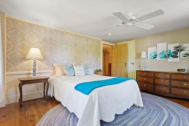 bedroom with wood finished floors, wallpapered walls, and ceiling fan