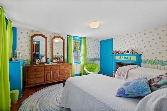 bedroom with wallpapered walls, wood finished floors, and a fireplace