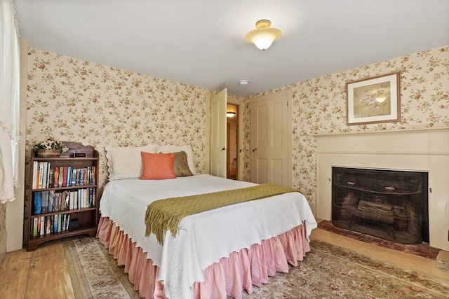 bedroom featuring wallpapered walls, light wood-style floors, and a fireplace