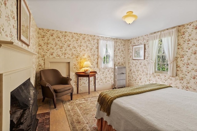 bedroom with radiator heating unit, hardwood / wood-style floors, wallpapered walls, and a fireplace with flush hearth