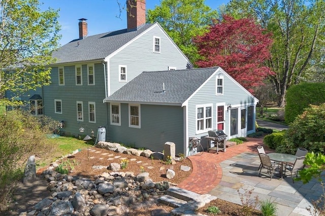 rear view of house with a chimney, a patio, and a shingled roof