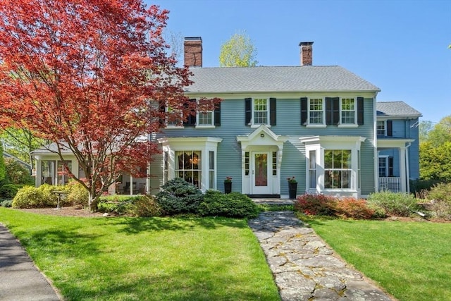colonial home featuring a chimney and a front lawn