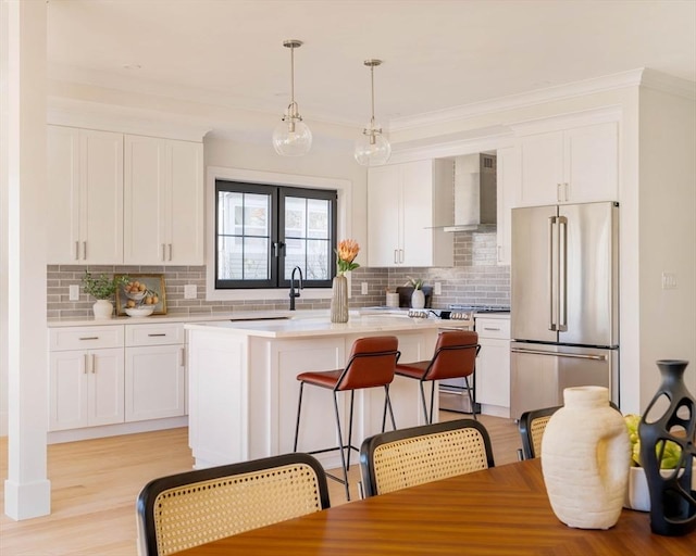 kitchen featuring white cabinetry, wall chimney exhaust hood, stainless steel appliances, decorative light fixtures, and a kitchen island