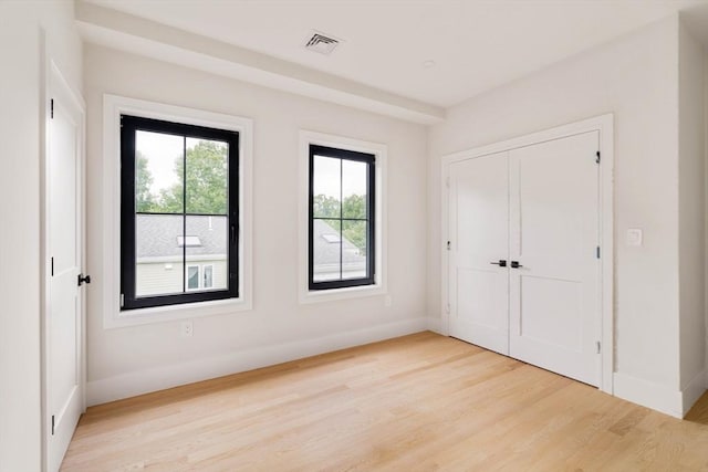 unfurnished bedroom with a closet, light hardwood / wood-style floors, and multiple windows