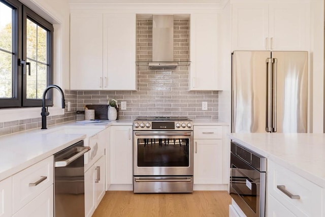 kitchen with white cabinets, wall chimney range hood, decorative backsplash, light hardwood / wood-style floors, and stainless steel appliances