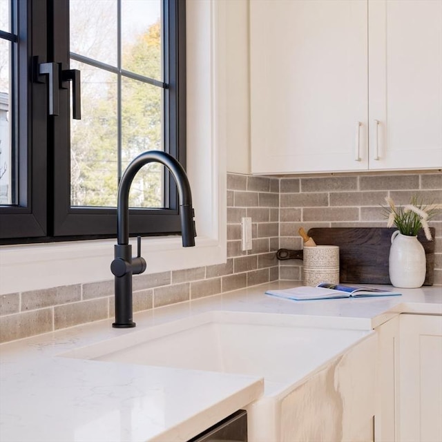 interior details featuring white cabinets, decorative backsplash, light stone countertops, and sink