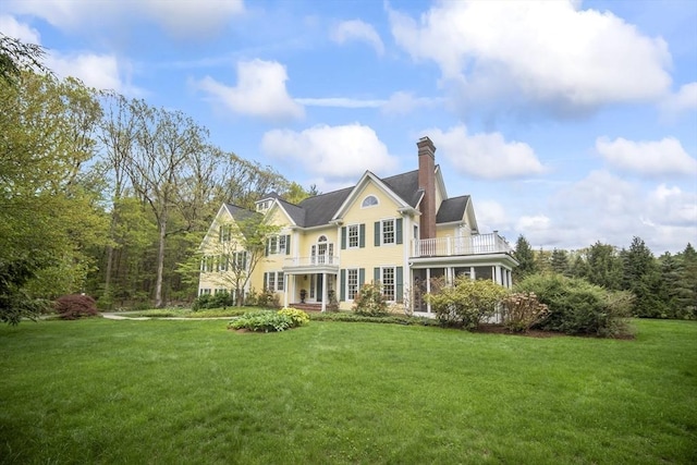 rear view of property featuring a balcony, a lawn, and a chimney