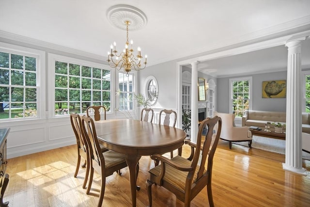 dining room featuring ornate columns, light wood-type flooring, crown molding, a fireplace, and a chandelier