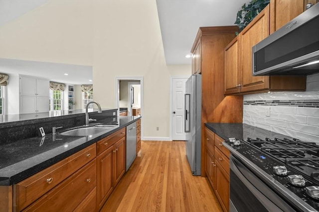 kitchen featuring stainless steel appliances, a sink, light wood-type flooring, brown cabinets, and dark stone countertops