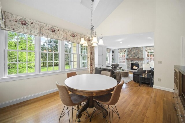 dining space with plenty of natural light, light wood-type flooring, baseboards, a fireplace, and high vaulted ceiling