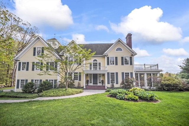 back of property with a balcony, a chimney, and a yard