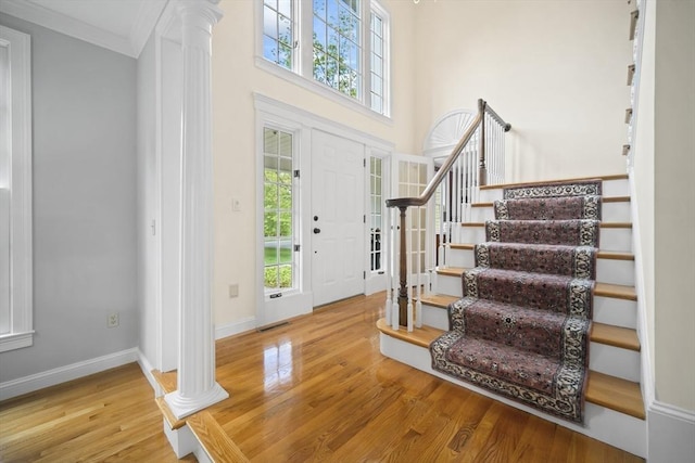 entrance foyer featuring decorative columns, wood finished floors, stairway, crown molding, and baseboards