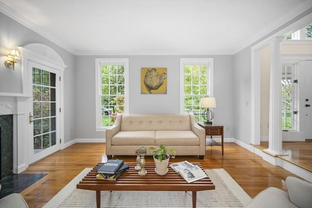 living area featuring decorative columns, plenty of natural light, wood finished floors, and crown molding