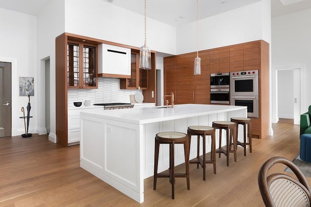 kitchen with pendant lighting, a center island with sink, stainless steel appliances, and a high ceiling