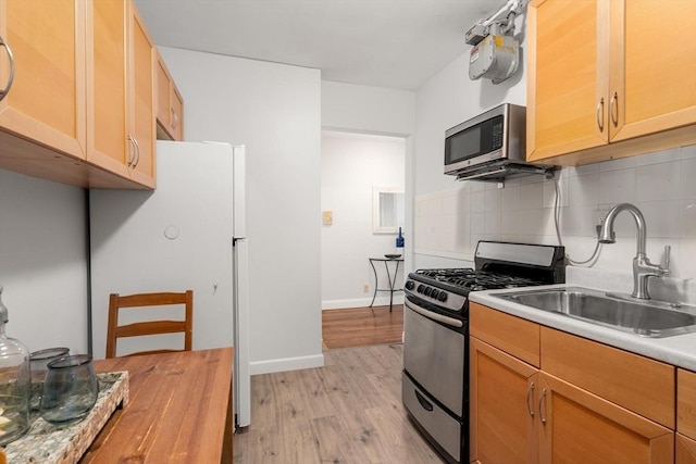 kitchen featuring backsplash, light wood-type flooring, light countertops, stainless steel appliances, and a sink