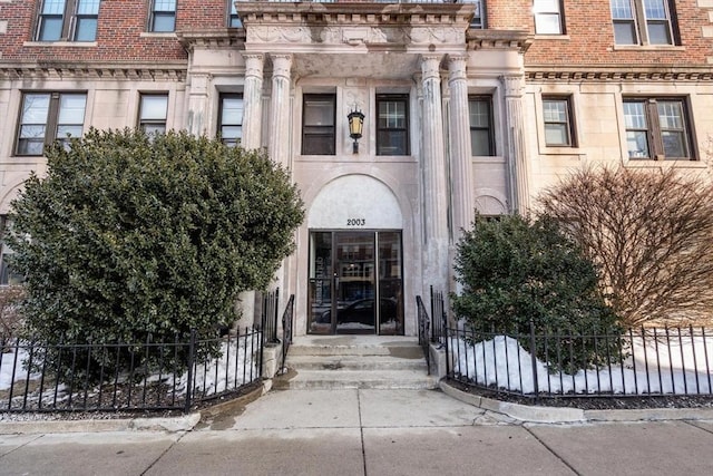 entrance to property featuring fence and brick siding