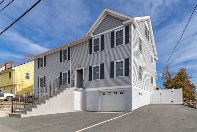 view of front facade featuring aphalt driveway, stairway, an attached garage, and a gate