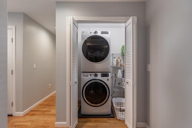 washroom featuring stacked washer / dryer, laundry area, light wood-type flooring, and baseboards