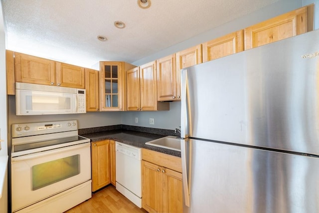 kitchen featuring glass insert cabinets, a sink, dark countertops, white appliances, and a textured ceiling