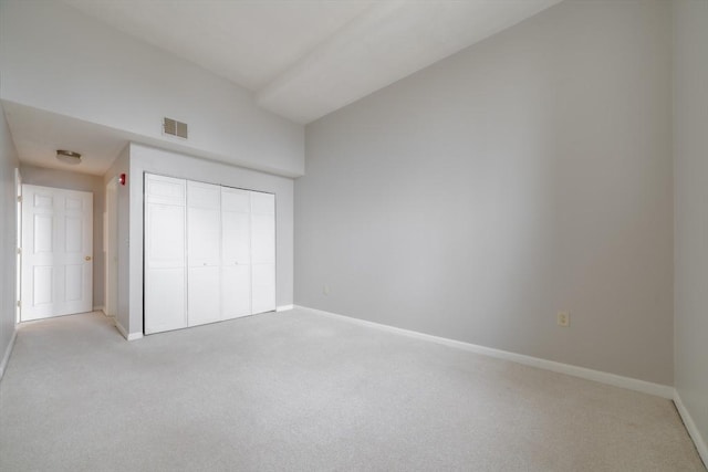 unfurnished bedroom featuring a closet, visible vents, light carpet, lofted ceiling, and baseboards