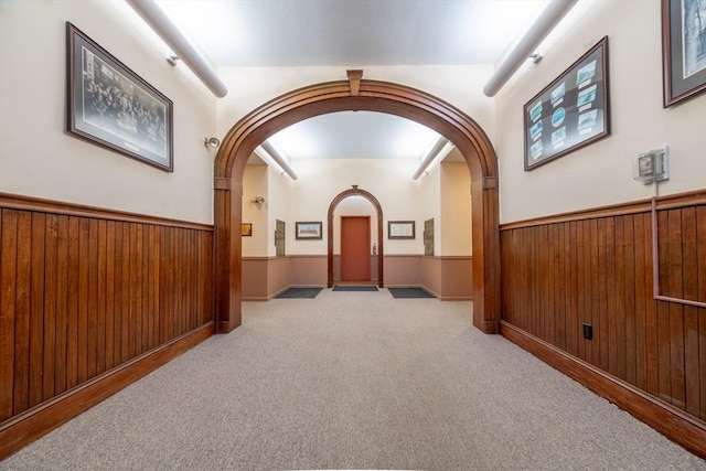hallway featuring arched walkways, wood walls, wainscoting, and carpet floors