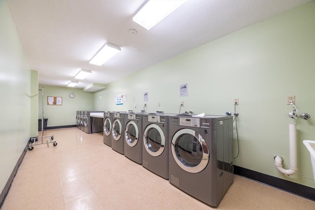 common laundry area featuring a textured ceiling, washing machine and clothes dryer, baseboards, and light floors