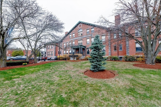 exterior space featuring brick siding, a chimney, and a front lawn
