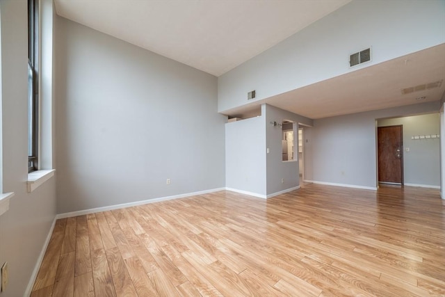 spare room with light wood finished floors, visible vents, baseboards, and lofted ceiling