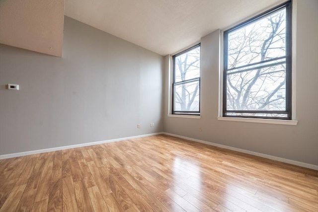 spare room featuring baseboards, light wood finished floors, and vaulted ceiling