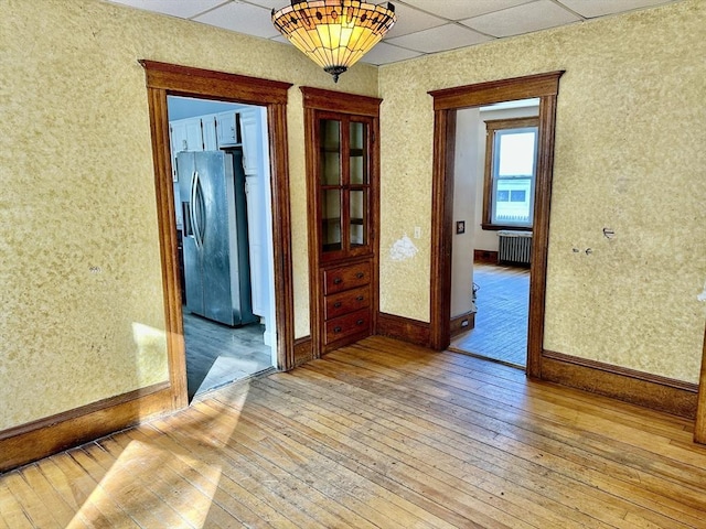 interior space with a paneled ceiling, radiator heating unit, and light hardwood / wood-style flooring