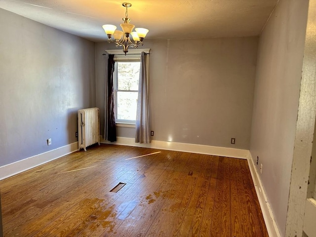 unfurnished room featuring wood-type flooring, radiator heating unit, and an inviting chandelier