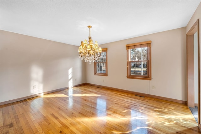 unfurnished room featuring a notable chandelier and light wood-type flooring