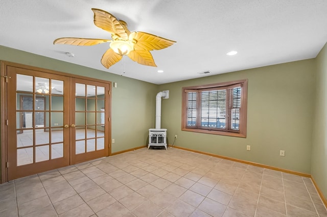 spare room featuring light tile flooring, ceiling fan, a wood stove, and french doors