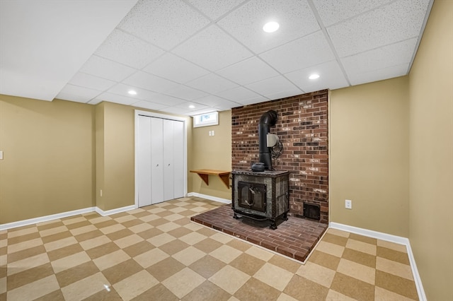 unfurnished living room with brick wall, light tile flooring, a drop ceiling, and a wood stove