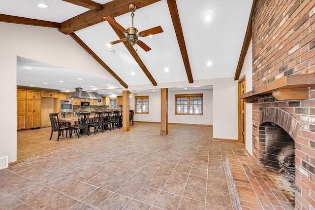 tiled living room with ceiling fan, a brick fireplace, vaulted ceiling with beams, and decorative columns