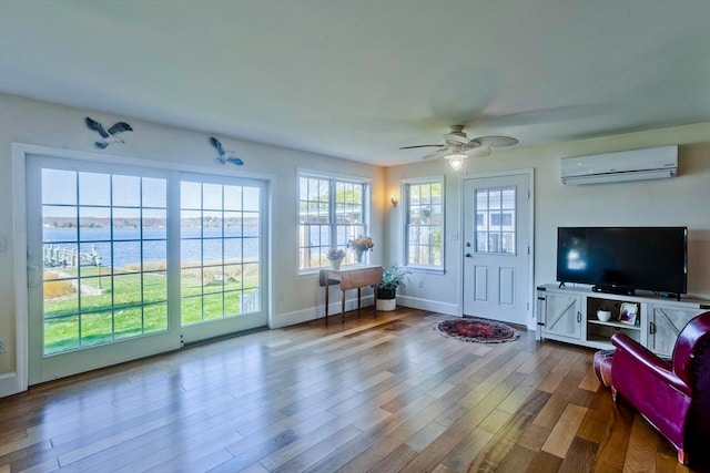 living room with a water view, a wall unit AC, ceiling fan, and wood-type flooring