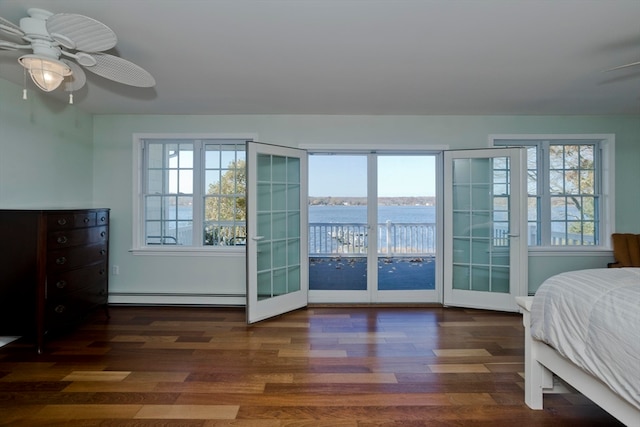 bedroom featuring a baseboard heating unit, a water view, dark wood-type flooring, ceiling fan, and multiple windows