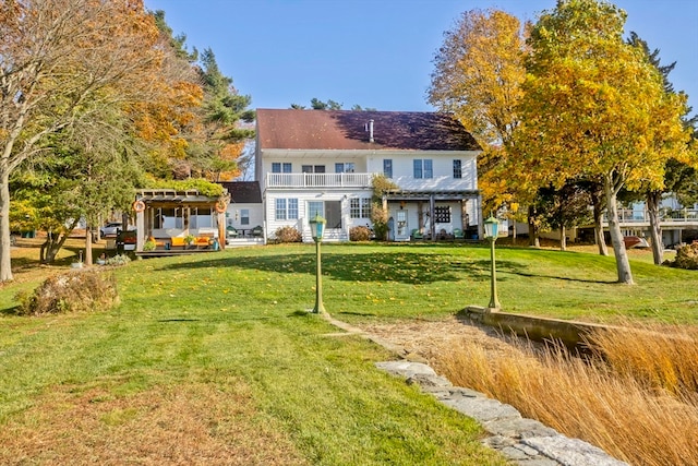 rear view of house with a balcony, a yard, and a pergola