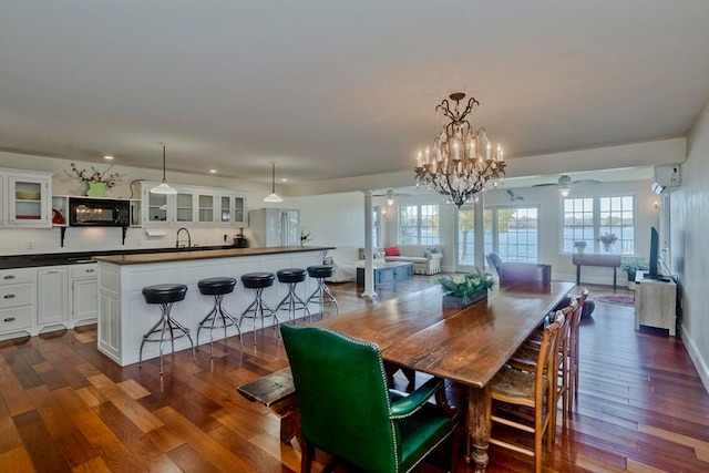 dining room with an AC wall unit, ornate columns, dark hardwood / wood-style floors, and ceiling fan with notable chandelier