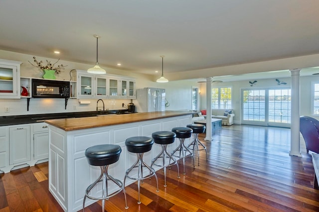 kitchen featuring wooden counters, ornate columns, dark hardwood / wood-style flooring, white cabinets, and hanging light fixtures