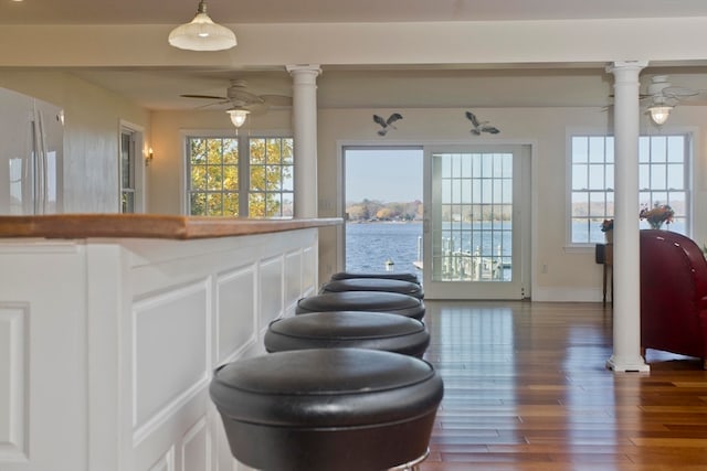 interior space with hardwood / wood-style flooring, ceiling fan, ornate columns, and a water view