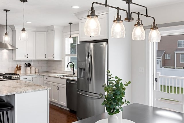 kitchen featuring pendant lighting, appliances with stainless steel finishes, white cabinets, a sink, and light stone countertops