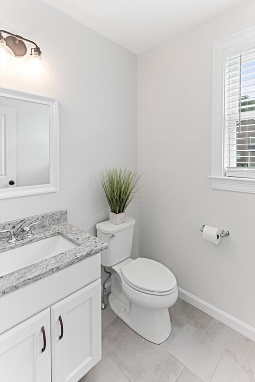 half bathroom featuring vanity, toilet, and baseboards