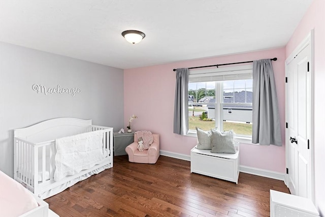 bedroom with a crib, baseboards, and dark wood-style flooring